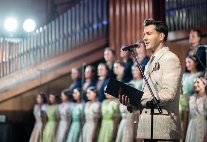 Na pierwszym planie Serghei Staruhin, który jest prowadzącym wydarzenie, a za nim chór w stylowych kostiumach z XIX w.