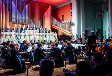 Na scenie Artyści chóru w kostiumach stylowych z końca XIX w. a przed nimi na dole sceny Orkiestra pod dyrekcją maestro Jacka Bonieckiego