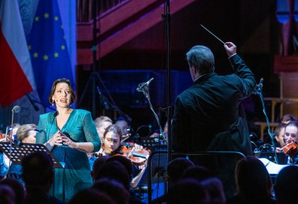 Na pierwszym planie Solistka a przed nią Dyrektor Jacek Boniecki trzymający w górze batutę