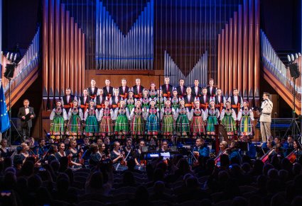 Na pierwszym planie Artyści w kostiumach łowickich na scenie a niżej Orkiestra pod dyrekcją maestro Jacka Bonieckiego