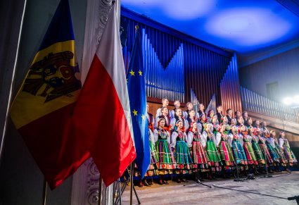 Na pierwszym planie flaga Polski, Mołdawii i Unii Europejskiej a na scenie Artyści chóru w kostiumach łowickich