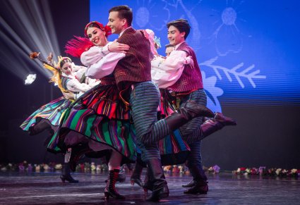 Pary Artystów w kostiumach opoczyńskich z zespołu "Mazowsze" podczas wykonywania choreografii tanecznej na scenie