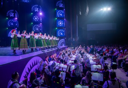 Na scenie Artystki z zespołu "Mazowsze" w kostiumach kurpiowskich, widoczna orkiestra obydwu zespołów
