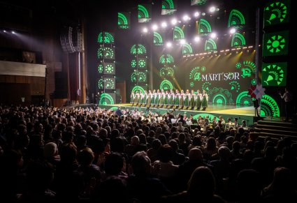 Na scenie Artyści chóru w kostiumach kurpiowskich, widoczna publiczność