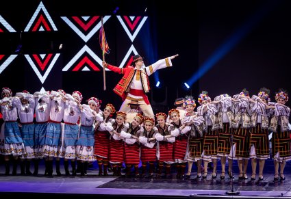 Grupa Artystów z zespołu Baletul Național JOC w kostiumach ludowych w trakcie wykonywania choreografii tanecznej na scenie