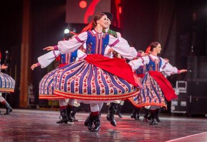 Na pierwszym planie na scenie Artystka z zespołu "Mazowsze" w kostiumie spiskim, na drugim reszta Artystów