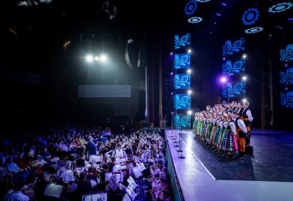 Na scenie Artyści chóru w kostiumach łowickich z zespołu "Mazowsze", widoczna Orkiestra z obydwu zespołów, widoczna również publiczność