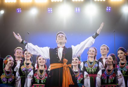 Zbliżenie na Solistę w kostiumie łowickim, w tle Artyści chóru również w kostiumach łowickich