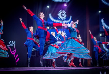 Pary Artystów z zespołu "Mazowsze" w kostiumach kujawskich na w scenie w trakcie wykonywania choreografii tanecznej
