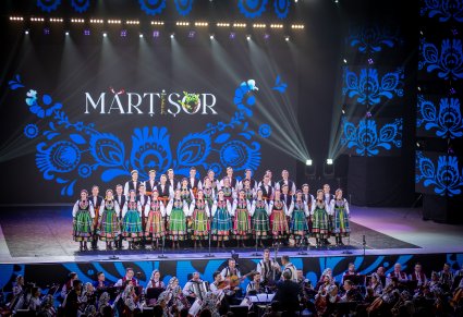 Na scenie Chór zespołu "Mazowsze" w kostiumach łowickich ustawiony w rzędy, Widoczna część orkiestry obydwu zespołów