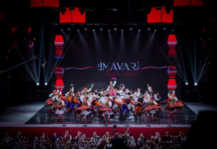 Na scenie Artyści zespołu "Mazowsze" wraz z Artystami Baletul Național JOC w kostiumach ludowych wykonujący choreografię taneczną, widoczna część orkiestry obu zespołów