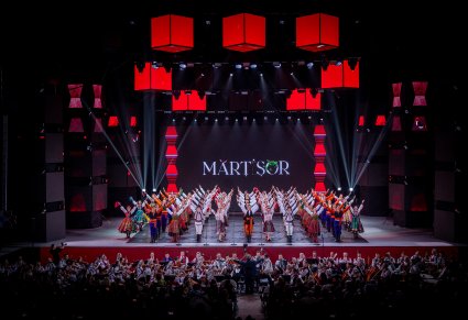 Na scenie Artyści zespołu "Mazowsze" wraz z Artystami zespołu Baletul Național JOC w trakcie wykonywania choreografii tanecznej, niżej orkiestra dwóch zespołów