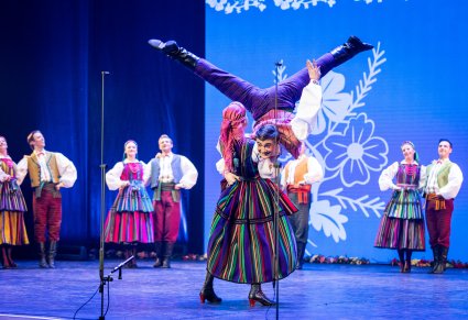 Na pierwszym planie para Artystów w kostiumach opoczyńskich w trakcie wykonywania spektakularnej choreografii tanecznej na scenie