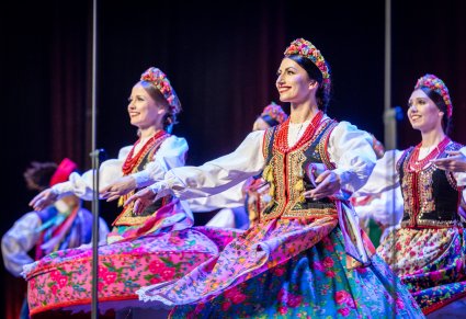 Zbliżenie na Artystki z zespołu "Mazowsze" w kostiumach krakowskich w trakcie wykonywania choreografii tanecznej na scenie