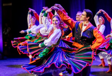 Zbliżenie na pary Artystów z zespołu "Mazowsze" w kostiumach sannickich podczas wykonywania choreografii tanecznej na scenie
