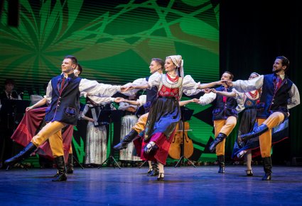 Grupa tancerzy w kostiumach ludowych podczas wykonywania choreografii tanecznej na scenie