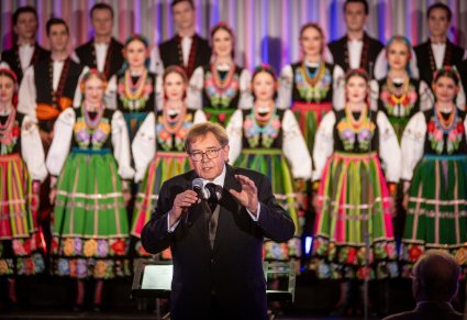 Zbliżenie na dyrygenta podczas przemowy, w tle widoczny chór