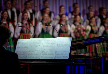 Zbliżenie na fortepian i nuty podczas koncertu, w tle widoczny chór