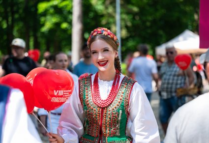 Artystka Zespołu Mazowsze w kostiumie ludowym trzymająca czerwone balony w kształcie serca