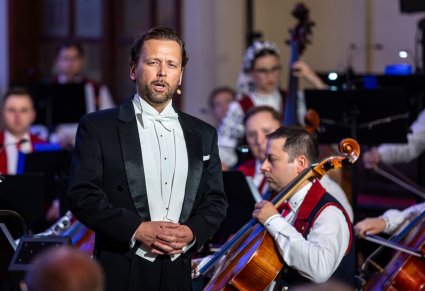 Zbliżenie na Solistę ubranego we frak a za nim część orkiestry