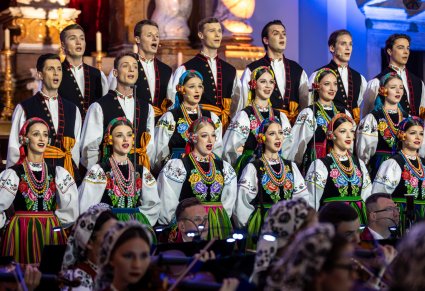 Artyści chóru w kostiumach łowickich ustawionych w rzędzie na dole zdjęcia widoczna orkiestra