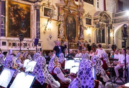 Na pierwszym planie Muzycy z orkiestry zwróceni w stronę Dyrektora Jacka Bonieckiego. Wnętrze pomieszczenia jest bogato zdobione