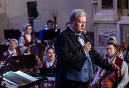 Dyrektor Jacek Boniecki wygłaszający mowę do mikrofonu, w tle część orkiestry