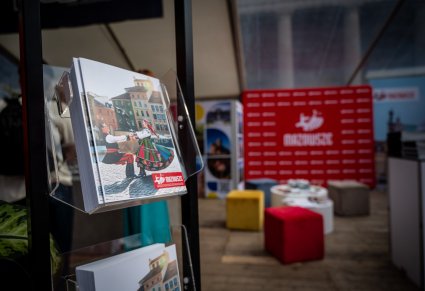 Na pierwszym planie artykuły marketingowe w formie ulotek, w tle czerwona ścianka z logo MAZOWSZE