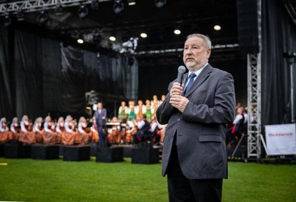 Przemawiająca osoba przed koncertem, w tle scena i zespół "Mazowsze"