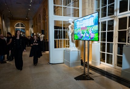 Ekran stojący w holu na którym wyświetla się film reklamowy zespołu "Mazowsze"