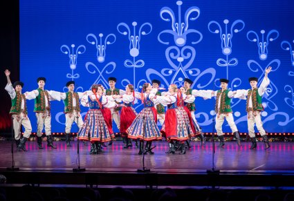 Grupa Artystów w kostiumach spiskich w trakcie wykonywania choreografii tanecznej na scenie