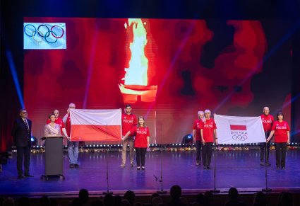 Olimpijczycy na scenie trzymają flagę olimpijską i flagę Polski
