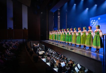 Artyści chóru Mazowsza w kostiumach kurii białych śpiewają na scenie