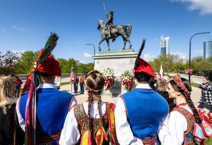 Dwie pary Artystów w kostiumach krakowskich zwróceni w stronę pomnika T. Kościuszki