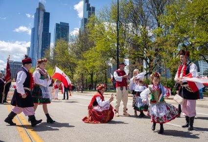 Grupa uczestników Parady Konstytucji 3 Maja w Chicago, ubrana w stroje krakowskie, trzymająca w flagę Polski