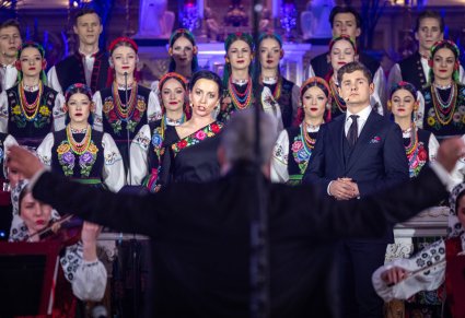 Na pierwszym planie Dyrygent zwrócony w stronę dwóch Solistów i Artystów Chóru