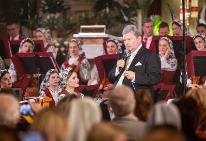 Dyrektor zespołu zwrócony w stronę publiczności, obok niego Muzycy z Orkiestry w kostiumach wilanowskich