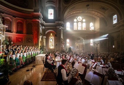 Widok z lewej strony ołtarza. Artyści Chóru w kostiumach łowickich, niżej Artyści Orkiestry w kostiumach wilanowskich, widoczna również publiczność koncertu, siedząca w ławach kościelnych