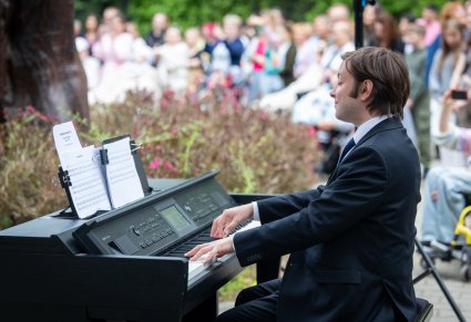 Zbliżenie na Akompaniatora grającego na instrumencie, w tle Publiczność konceru