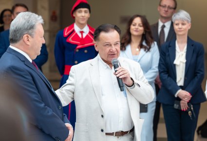 Marszałek Województwa Mazowieckiego wypowiadający się do mikrofonu, obok Dyrektor zespołu "Mazowsze", a w tle pracownicy wraz z Artystą w kostiumie wilanowskim