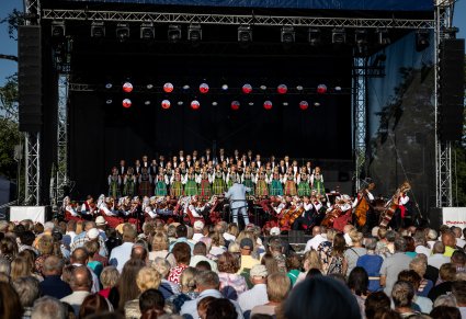 Chór, orkiestra i dyrygujący Dyrektor zespołu, na pierwszym planie część publiczności