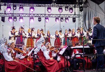 Na pierwszym planie częśc orkiesty z dyrygentem, w tle artyści baletu w kostiumach limanowskich