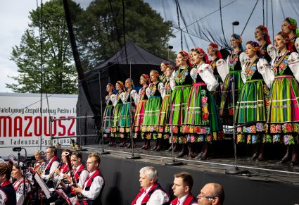 Widok na chór i solistki chóru w kostiumach łowickich, poniżej częśc orkiestry w kostiumach wilanowskich