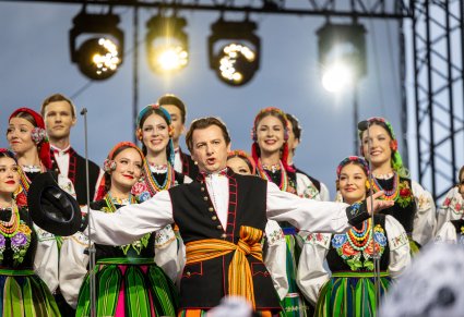 Na pierwszym planie artysta chóry w kostiumie łowickim, podczas wykonywania "Furmana", w tle część chóru także w kostiumach łowickich