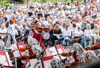 Zbliżenie na skrzypaczkę w kostiumie wilanowskich, przed skrzypaczką pozostała część orkiestry, za skrzypaczką widoczna zgromadzona publiczność