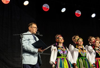 Prowadzący koncert- były Kierownik Chóru w trakcie wypowiedzi do mikrofonu, obok widoczna część Chóru w kostiumach łowickich