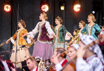 Na scenie Artystki w kontuszach w trakcie wykonywania choreografii tanecznej, niżej widoczna część orkiestry w kostiumach wilanowskich