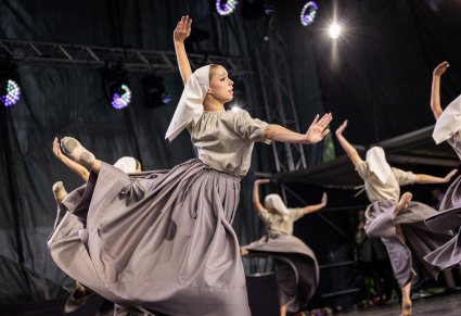 Zbliżenie na Artystę w szarym stylizowanym kostiumie w trakcie wykonywania choreografii tanecznej