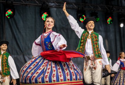Na pierwszym planie para Artystów w kostiumach spiskich w trakcie wykonywania choreografii tanecznej