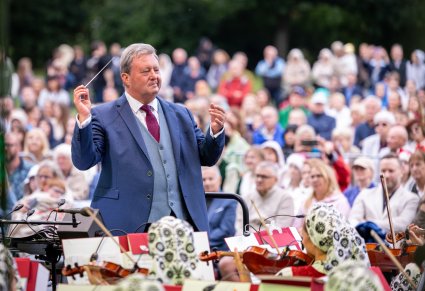 Zbliżenie na Dyrygenta, który trzyma w ręku batutę, w tle widoczna Publiczność
